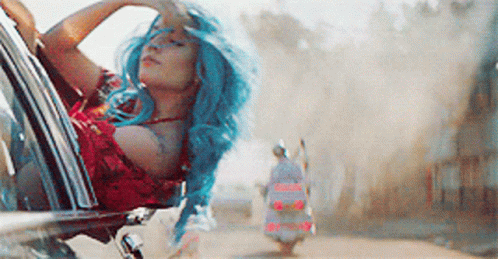 A Woman With Blue Hair Is Sitting In A Car Looking Out The Window GIF