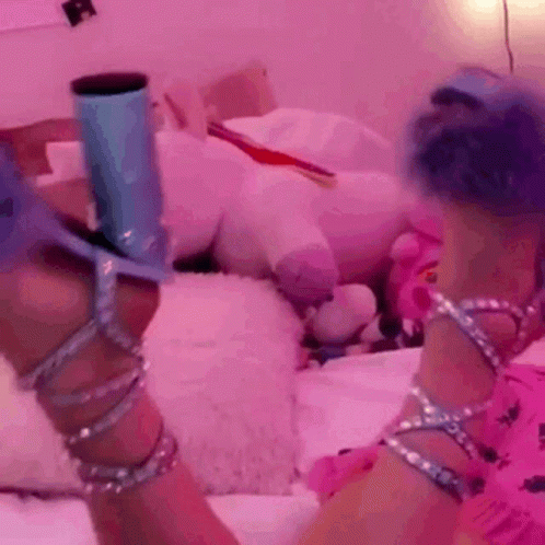 A Woman With Blue Hair Is Sitting On A Bed Wearing A Pair Of Heels GIF