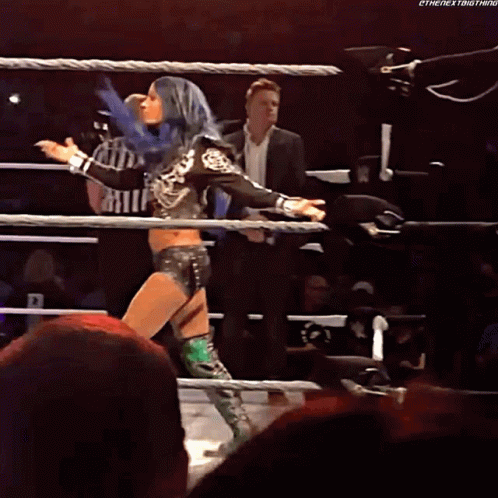 A Woman With Blue Hair Is Standing In A Wrestling Ring While A Referee Watches GIF