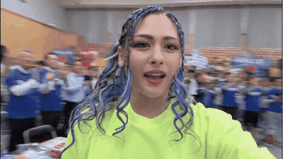 A Woman With Blue Hair Is Taking A Selfie In Front Of A Crowd . GIF