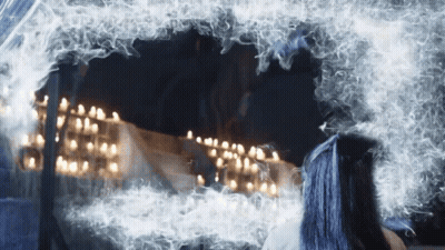 A Woman With Blue Hair Looks At Herself In A Mirror GIF