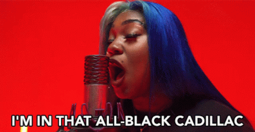 A Woman With Blue Hair Singing Into A Microphone With The Words I 'M In That All Black Cadillac Below Her GIF