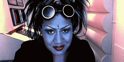 A Woman With Blue Paint On Her Face And Goggles On Her Head Looks At The Camera . GIF
