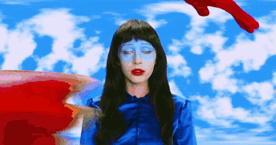 A Woman With Blue Paint On Her Face Stands In Front Of A Blue Sky With Clouds GIF