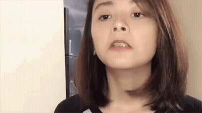 A Woman With Braces On Her Teeth Is Making A Funny Face While Standing In Front Of A Refrigerator . GIF