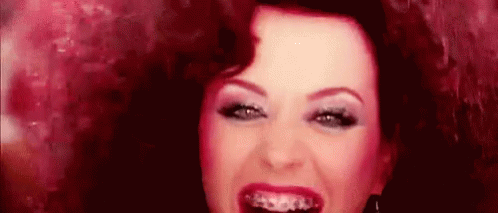 A Woman With Braces On Her Teeth Is Smiling And Looking At The Camera . GIF