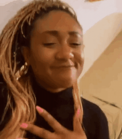 A Woman With Braids And Pink Nails Is Making A Funny Face . GIF