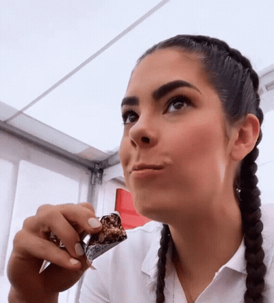A Woman With Braids Is Eating A Piece Of Chocolate GIF