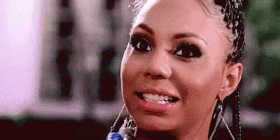 A Woman With Braids Is Smiling And Looking At The Camera . GIF