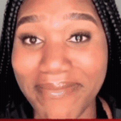 A Woman With Braids Is Smiling And Looking At The Camera . GIF