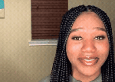 A Woman With Braids Is Smiling And Looking At The Camera In Front Of A Window . GIF