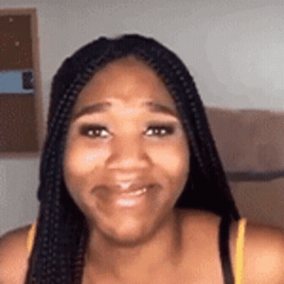 A Woman With Braids Is Smiling For The Camera In A Room . GIF
