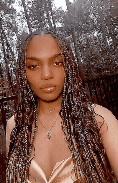 A Woman With Braids Is Wearing A Necklace And A Gold Top GIF