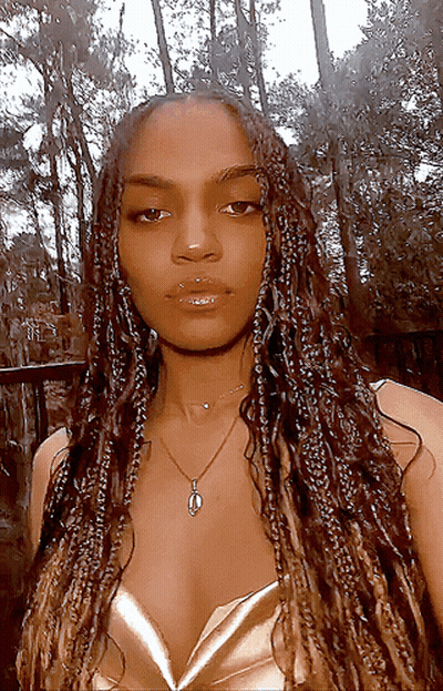 A Woman With Braids Is Wearing A Necklace And A Gold Top GIF