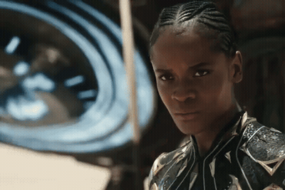 A Woman With Braids Looks At The Camera In Front Of A Large Clock GIF