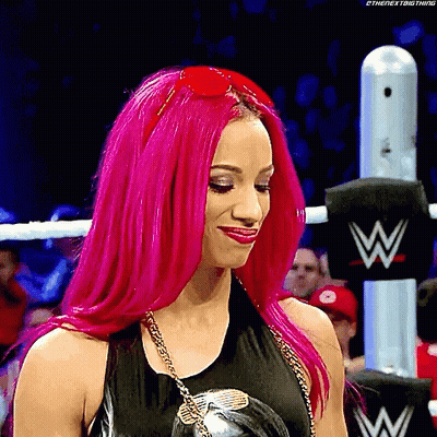 A Woman With Bright Pink Hair Is Standing In A Wrestling Ring Wearing Sunglasses . GIF