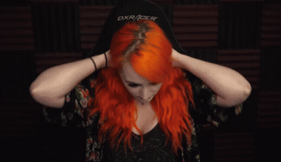 A Woman With Bright Red Hair Is Holding Her Hair In Her Hands . GIF