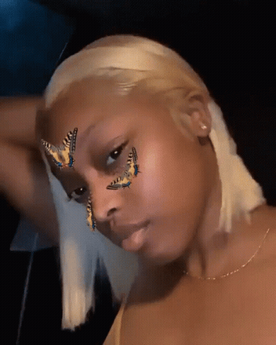 A Woman With Butterflies Painted On Her Face Looks At The Camera GIF