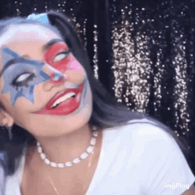 A Woman With Clown Makeup On Her Face Is Smiling And Looking At The Camera . GIF