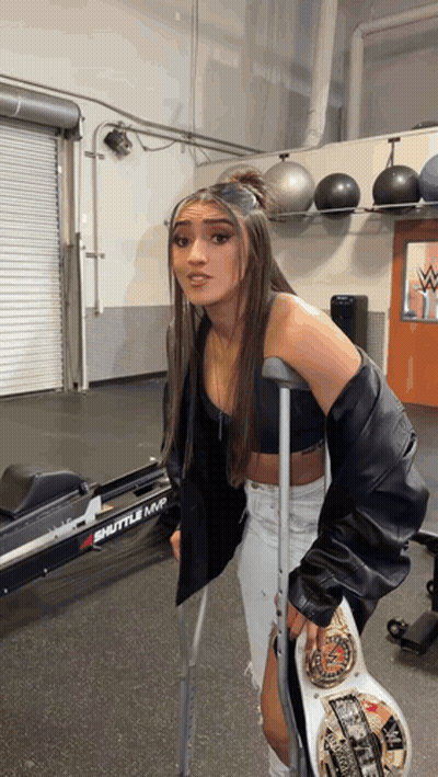 A Woman With Crutches Holds A Wrestling Championship Belt In A Gym . GIF