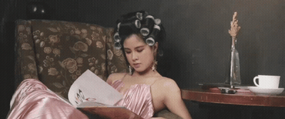 A Woman With Curlers In Her Hair Is Reading A Book GIF