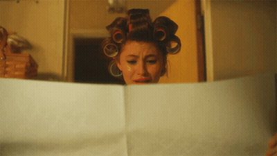 A Woman With Curlers On Her Head Is Reading A Piece Of Paper GIF