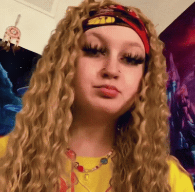 A Woman With Curly Blonde Hair Is Wearing A Headband And A Necklace . GIF