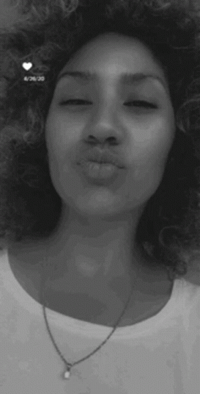 A Woman With Curly Hair And A Necklace Is Blowing A Kiss . GIF