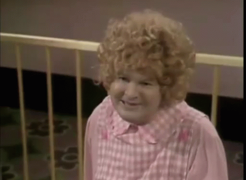 A Woman With Curly Hair And A Pink Shirt Is Standing Next To A Fence . GIF