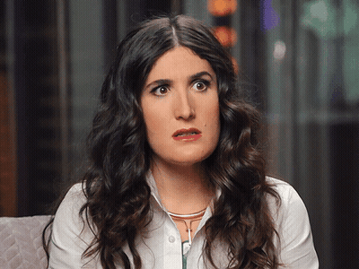 A Woman With Curly Hair And A White Shirt Looks Surprised GIF