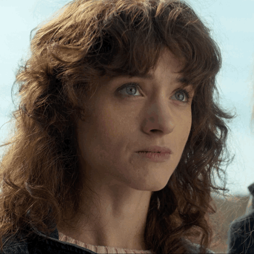 A Woman With Curly Hair And Blue Eyes Looks At The Camera GIF