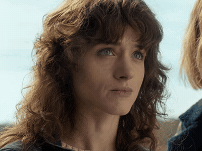 A Woman With Curly Hair And Blue Eyes Looks At The Camera GIF