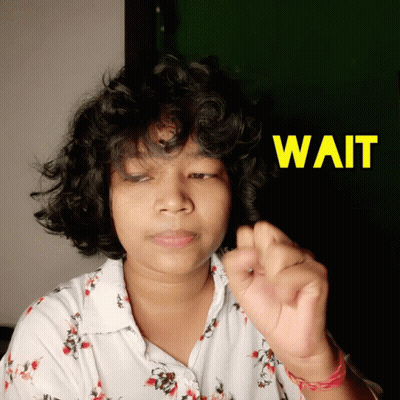 a woman with curly hair holds her hand up in front of a sign that says " wait "