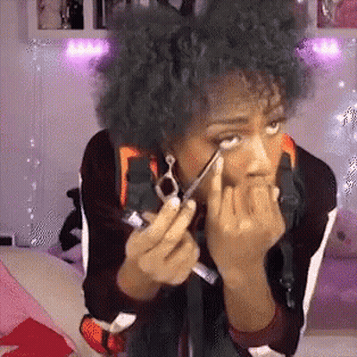 A Woman With Curly Hair Is Applying Eye Shadow To Her Eye With A Pair Of Scissors . GIF