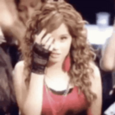 A Woman With Curly Hair Is Covering Her Face With Her Hand While Wearing Gloves . GIF