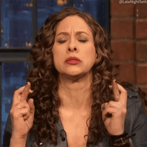 A Woman With Curly Hair Is Crossing Her Fingers And Making A Face GIF