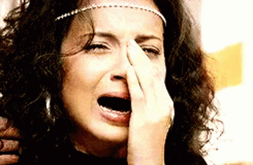 A Woman With Curly Hair Is Crying And Covering Her Nose With Her Hand GIF