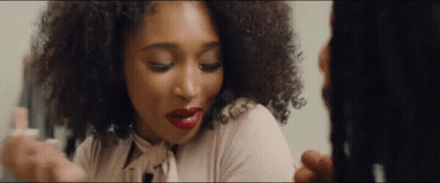 A Woman With Curly Hair Is Looking At Herself In A Mirror . GIF