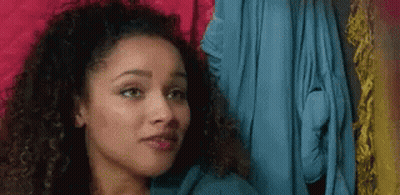 A Woman With Curly Hair Is Looking At The Camera While Standing In Front Of A Closet . GIF