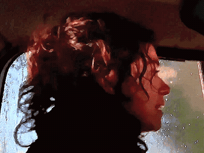 A Woman With Curly Hair Is Looking Out A Window GIF