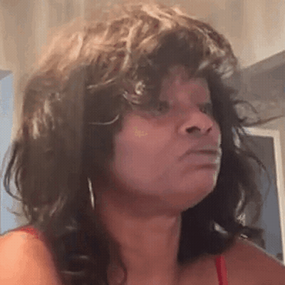 A Woman With Curly Hair Is Making A Funny Face And Looking At The Camera . GIF
