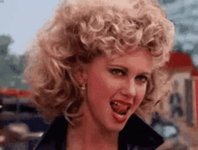 A Woman With Curly Hair Is Making A Funny Face With Her Tongue Hanging Out . GIF