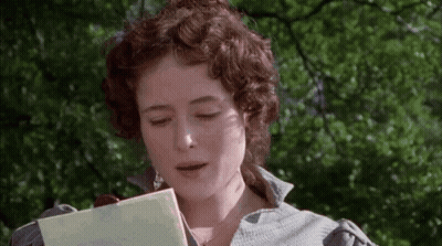 A Woman With Curly Hair Is Reading A Book In Front Of Trees . GIF