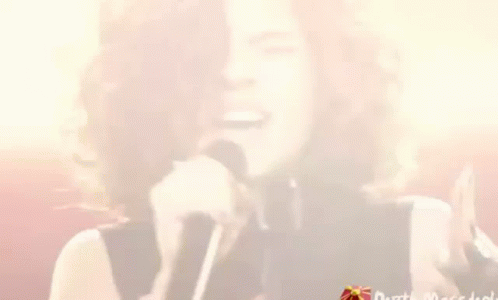 A Woman With Curly Hair Is Singing Into A Microphone While Winking . GIF