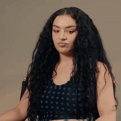 A Woman With Curly Hair Is Sitting In A Chair And Making A Funny Face . GIF