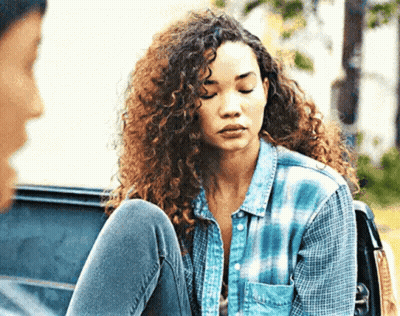 A Woman With Curly Hair Is Sitting In The Back Of A Car With Her Legs Crossed . GIF