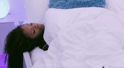 A Woman With Curly Hair Is Sleeping In A Bed With A White Blanket GIF