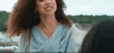 A Woman With Curly Hair Is Smiling And Looking At The Camera While Standing Next To Another Woman . GIF
