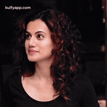 A Woman With Curly Hair Is Smiling And Looking To The Side . GIF