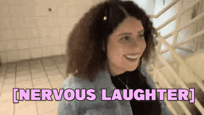 A Woman With Curly Hair Is Smiling And Says Nervous Laughter . GIF